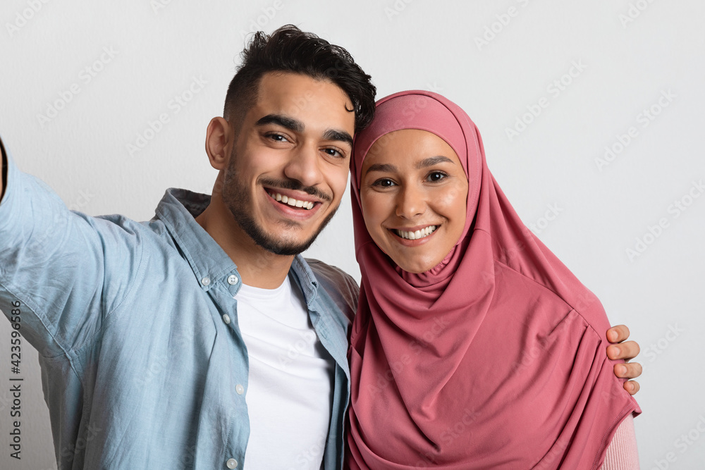 Cheerful Young Muslim Couple Taking Selfie Together, Happy Spouses Smiling At Camera