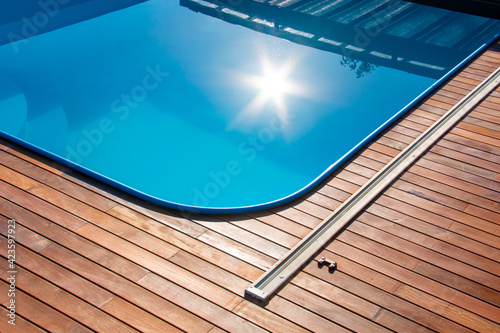 Ipe wood decking around the pool, edge of the outdoor swimming pool with sun reflection on the blue water, tropical hardwood deck close up