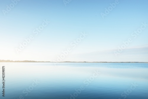Panoramic aerial view of the blue forest lake (river) at sunset. Soft sunlight, clear sky, reflections on water. Early spring. Idyllic pastoral landscape. Nature, environment, ecology, ecotourism