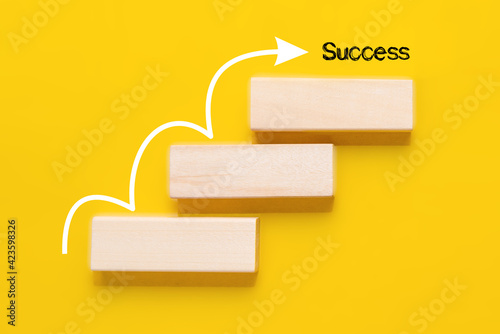 Wooden block stacking as stair with white arrow up on yellow background. Step for Success concept