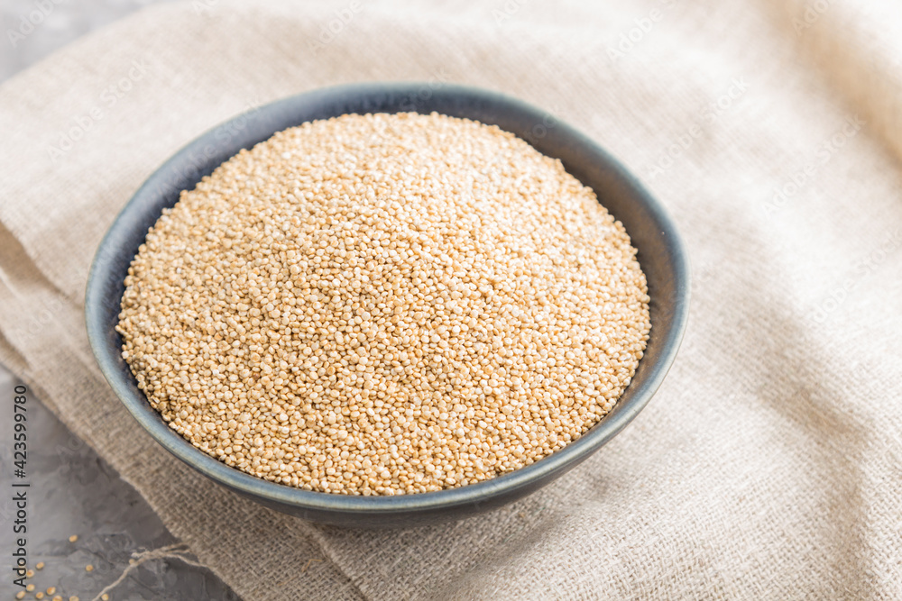 Blue ceramic bowl with raw white quinoa seeds on a gray concrete  background. Side view, selective focus.