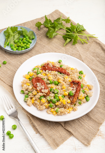 Quinoa porridge with green pea, corn and dried tomatoes on ceramic plate on a white wooden background. Side view.