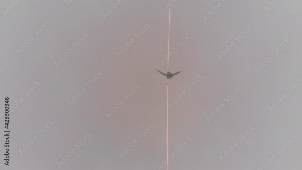 Top view of a man walking on a tight sling at a high altitude in the fog.