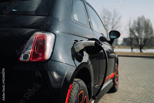 A compact black electric car charges up in a parking lot to maintain the environment. © marozzau