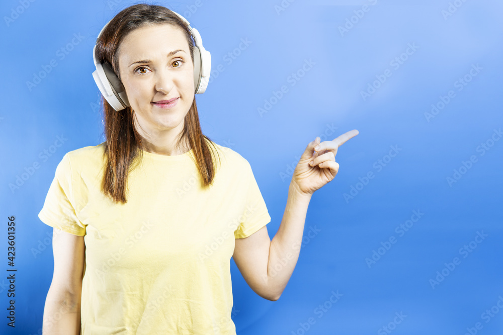 Obraz premium Smiling beautiful young woman pointing aside on blue background for design with copyspace