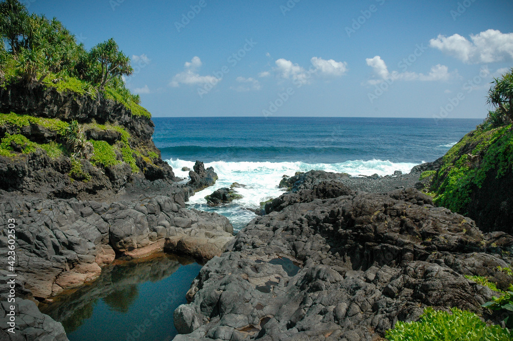 water flowing into lagoon surrounded by Black lava Rocks.  Waves from the Pacific Ocean.  Maui Hawaii USA
