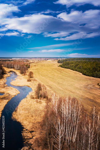 Fototapeta Naklejka Na Ścianę i Meble -  Forest landscape with sky, field and river. Spring sunny day, wild European nature. Beautiful sky. Top view, aerial photography. 