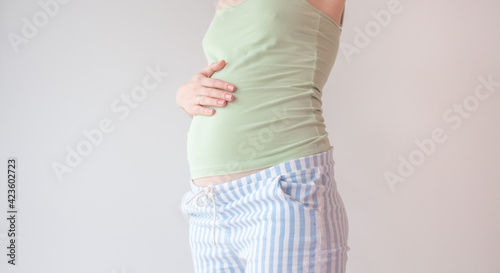 Pregnancy photo in the room during the day with lighting from the window. Pregnant mother holding her belly in anticipation of motherhood and childbirth