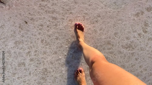 white with a pink tinge of salt or lime. the bottom of a salt lake, on which a thin layer of clear water runs along the woman's long bare slender legs. view from above photo