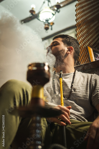 Young handsome guy smoking hookah alone closeup. Hookah and sparks from coals. Shisha, spark, hookah sparks. Young man smokes a fragrant oriental hookah.