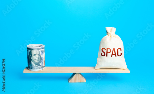 Bundle of dollars and a bag of SPAC on scales. The concept of attracting investors' money to fund the merger of companies into a new one. Assessing the value of the new company and profitability. photo