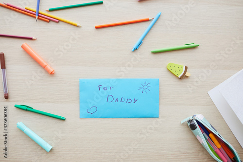 Top view background image of letter for dad with handmade gift on Fathers day set on table with colored crayons, copy space