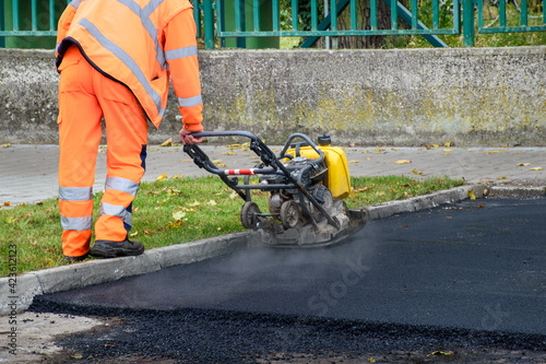 Foto Paving worker uses vibratory plate compactor to compact new asphalt near curbsto