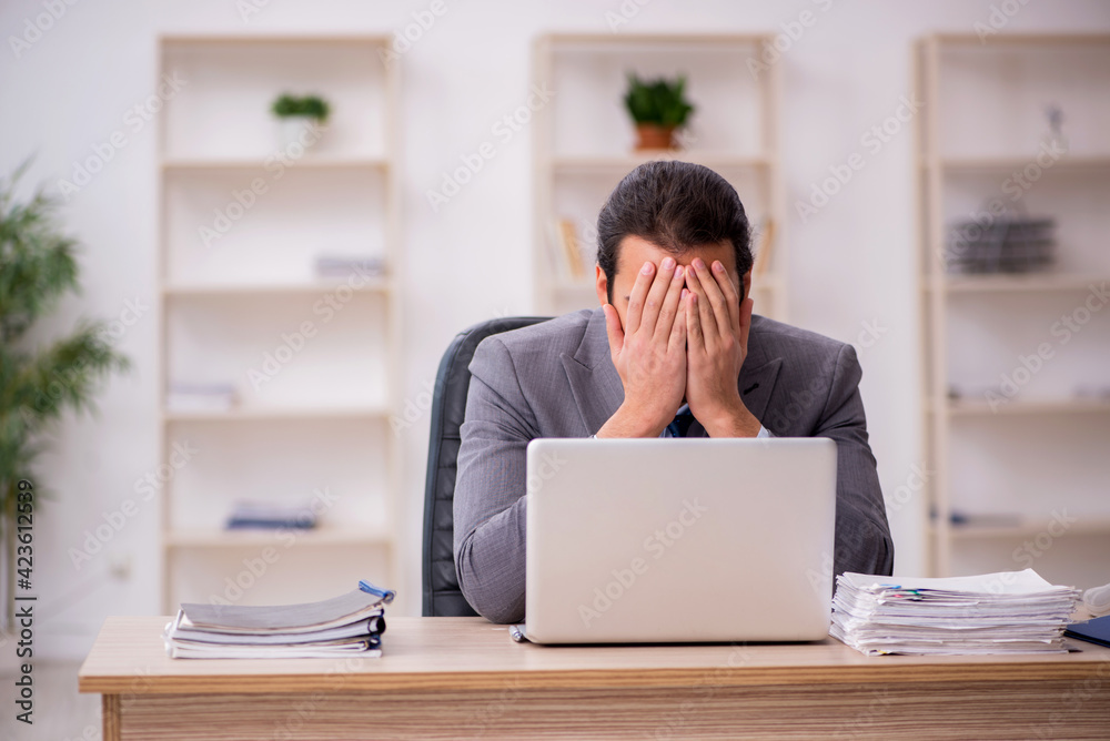 Young male employee unhappy with excessive work in the office Young male employee unhappy with excessive work in the office
