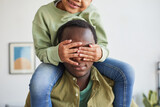 Cropped portrait of cute African-American girl sitting on fathers shoulders while playing together in cozy home interior