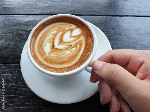 Male hand hold Cup of coffee with beautiful Latte art on wood table.