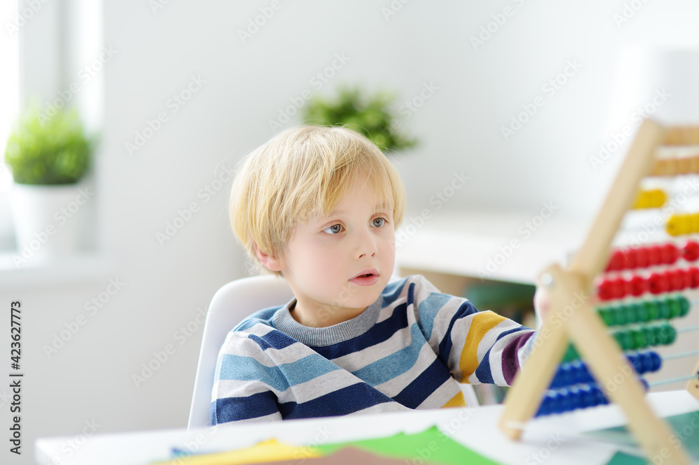 Elementary student boy doing homework at home. Child learning to count, solves arithmetic examples, doing exercises in workbook. Math tutorial. Preparing preschooler baby for school. Education Elementary student boy doing homework at home. Child learning to count, solves arithmetic examples, doing exercises in workbook. Math tutorial. Preparing preschooler baby for school. Education
