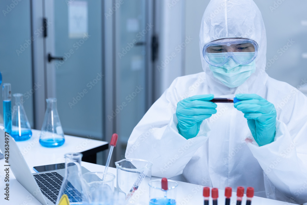 Asian man scientist is wearing Personal Protective Equipment (PPE) doing Medical Research looking at a blood sample and biochemical cell in laboratory. Medical experiment, COVID19 concept. Asian man scientist is wearing Personal Protective Equipment (PPE) doing Medical Research looking at a blood sample and biochemical cell in laboratory. Medical experiment, COVID19 concept.