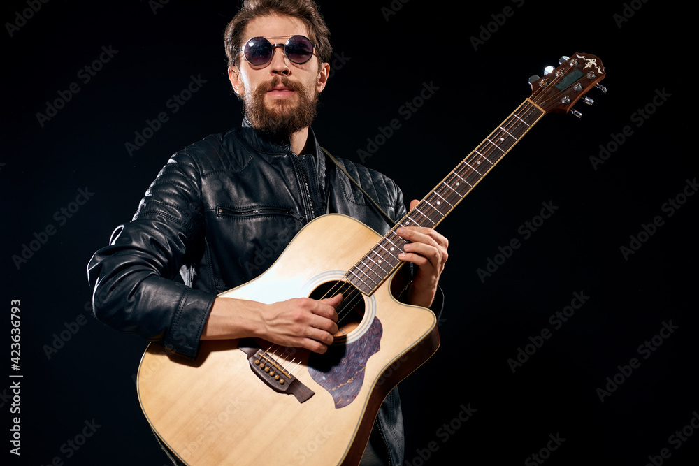 Obraz premium man with a guitar in his hands black leather jacket sunglasses music emotions black background