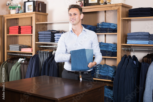 Smiling guy deciding on new trousers in male cloths store