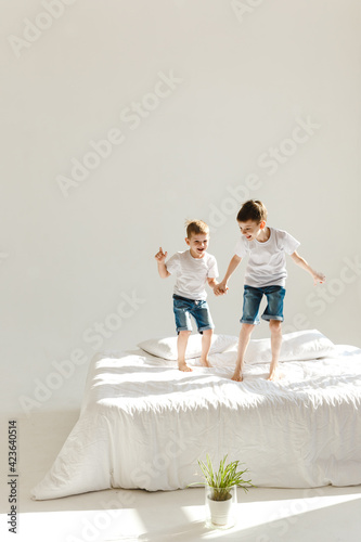 Indoor positive activity. Small children jumping on a bed and having fun in sunshine