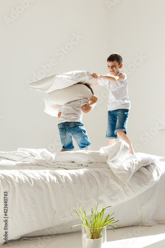 Indoor positive activity. Small children jumping on a bed and having fun fighting with pillows in sunshine