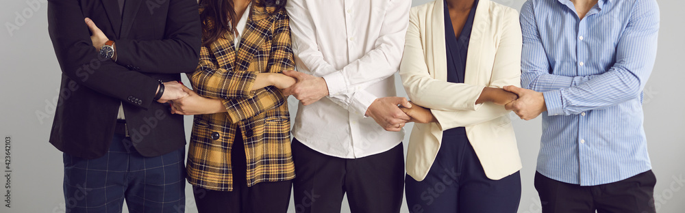 Multiracial men and women working in one company holding hands standing together in studio. Business associates, alliance, teamwork, team unity, corporate support concept. Conceptual background banner - obrazy, fototapety, plakaty 
