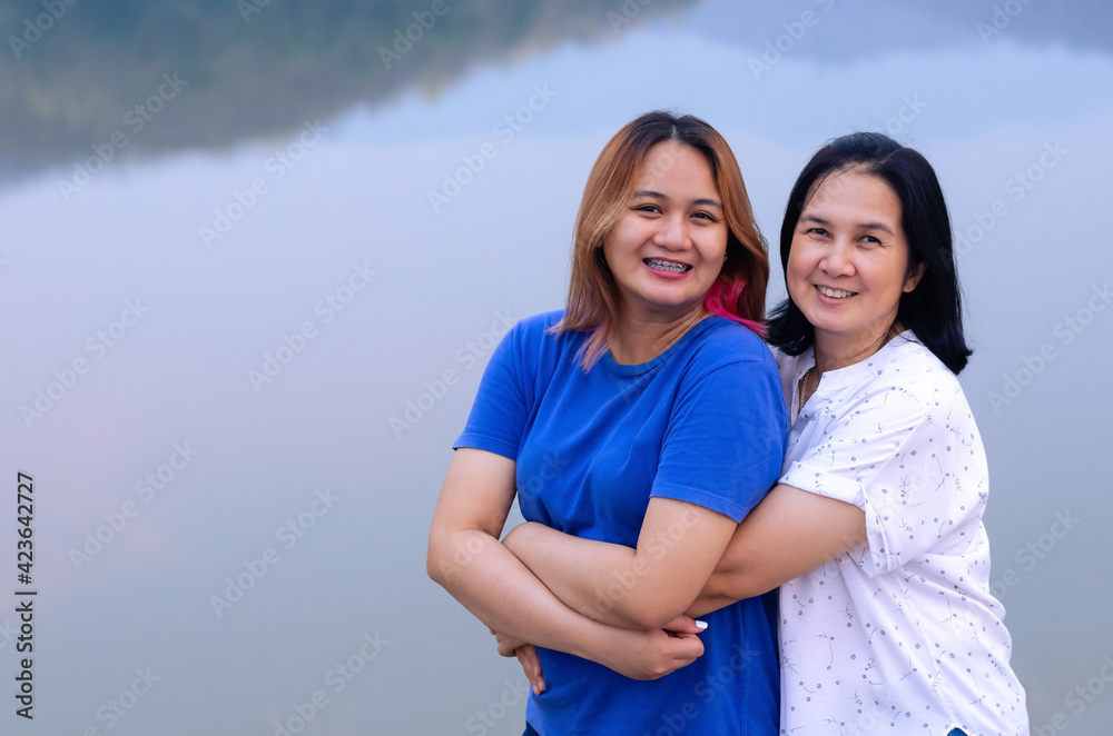 Single asian mother and her teenager daughter hugging together on lake background with shadow of mountain. Mother day concept
