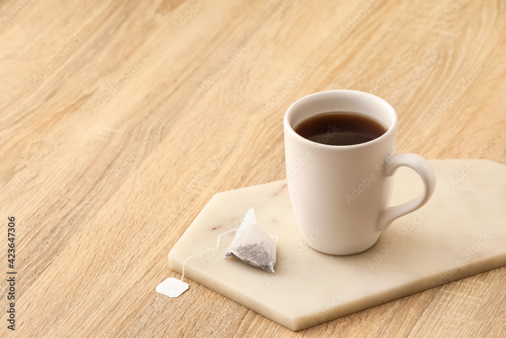Obraz premium Cup of hot aromatic beverage and tea bag on table