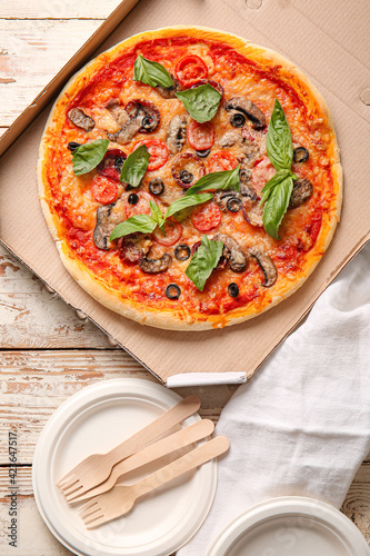 Cardboard box with tasty pizza on light wooden background