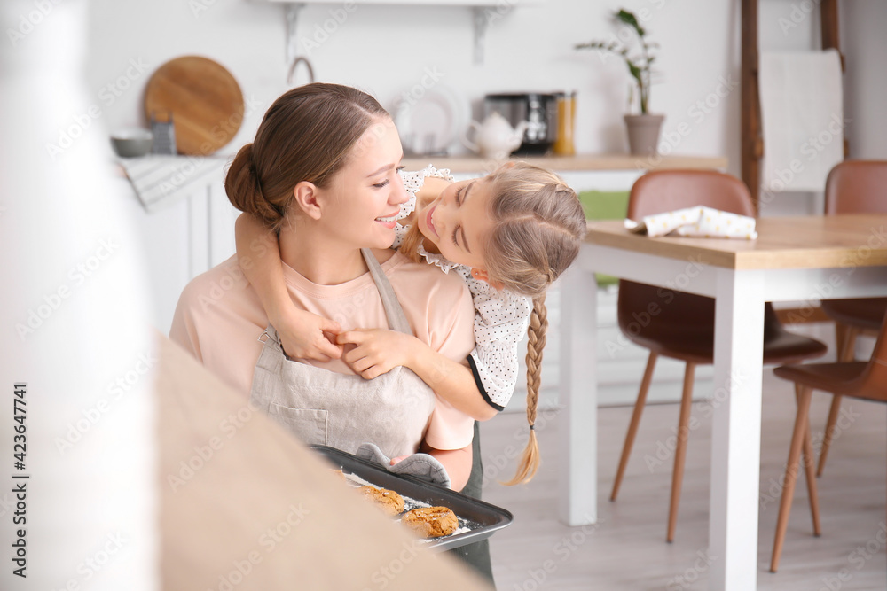 Happy woman and her little daughter baking cookies in kitchen