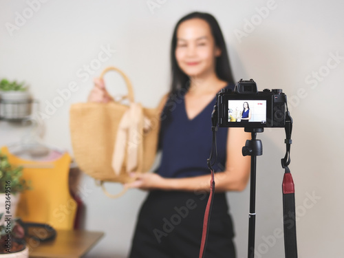 Asian woman working at home, using camera phone to live or record video selling her woven bag. Indoor, selective focus. Business and online selling concept.