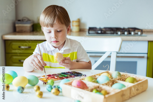 Caucasian boy paints Easter eggs with paints and brush. Preparing for Easter holiday