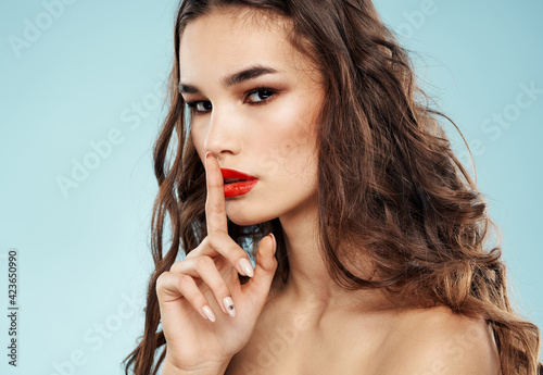 Beautiful woman model holds her finger near the face on a blue background and curly hair