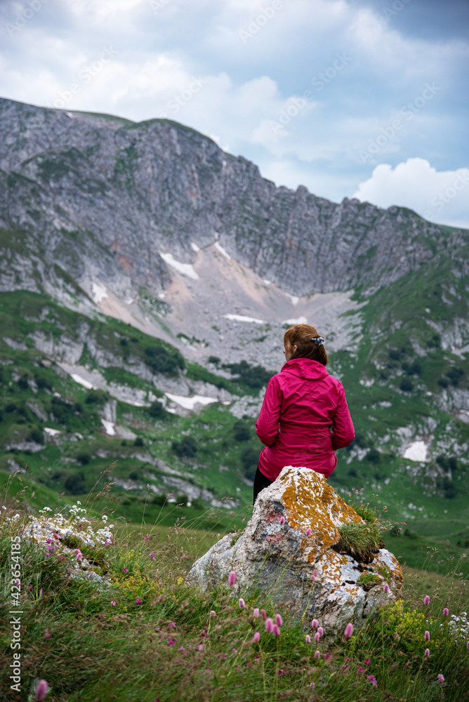 A women in a red jacket sits on a rock in a mountain valley and looks into the distance. Mountain landscape. Russia, Adygea