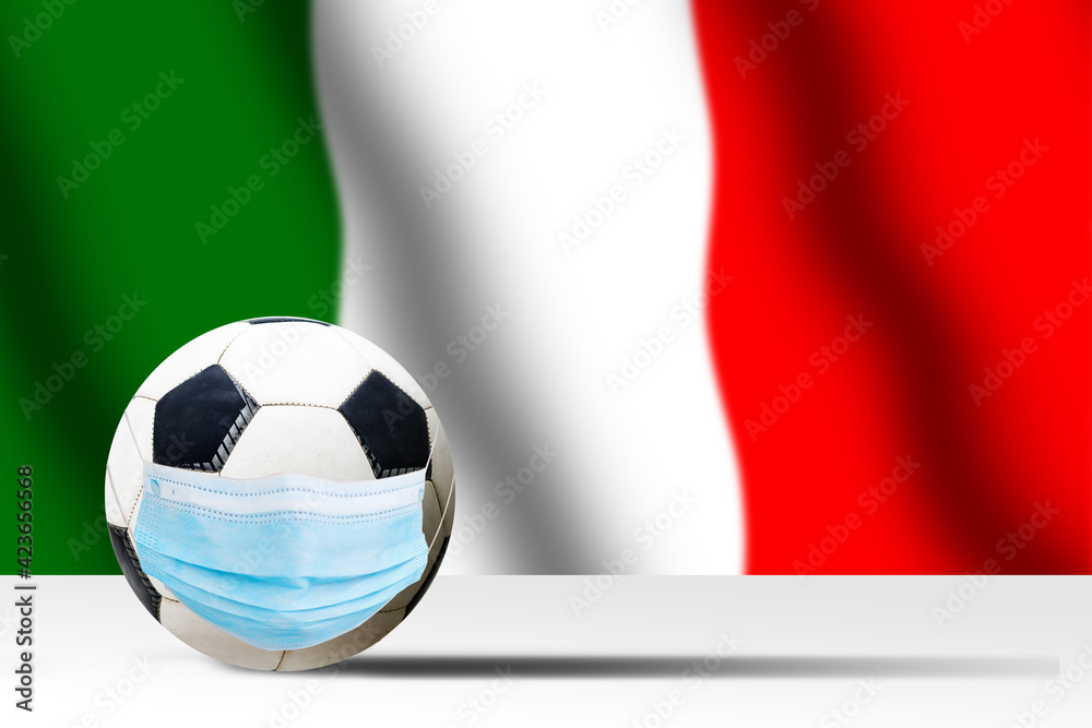 Soccer ball in a medical mask against the background of the flag of italy. Corona protection against viruses bacteria stop. Cancellation of sporting events. Copy space Soccer ball in a medical mask against the background of the flag of italy. Corona protection against viruses bacteria stop. Cancellation of sporting events. Copy space