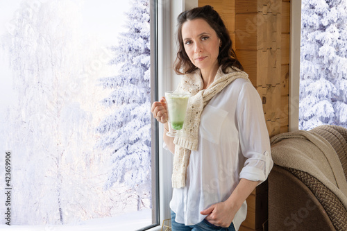 A woman stands at the window with a mug of drink