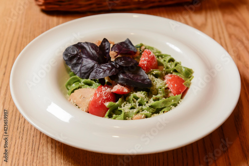 Tagliatelle pasta with pesto on light plate. Spinach macaroni with cheese and tomatoes over rustic wooden table.