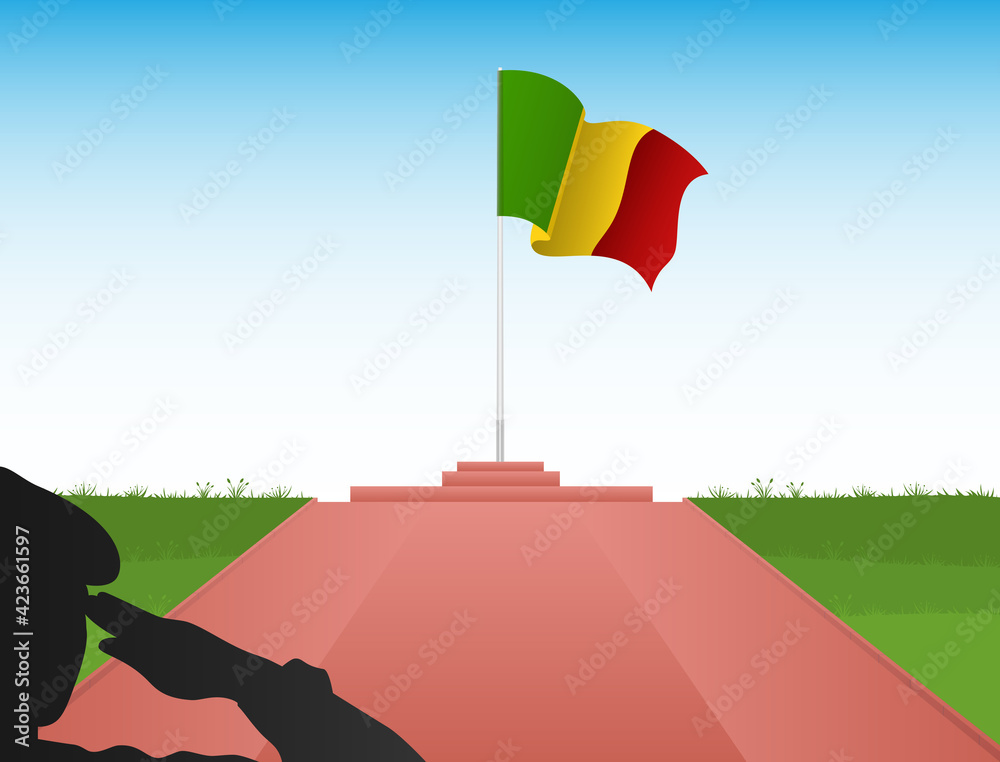 The flag of Mali flies above the pole in the shadow of a soldier saluting the flag