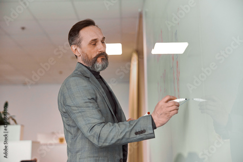 Caucasian adult man in office is writing on the glass desk