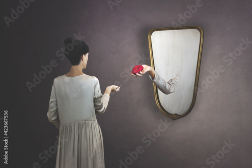 surreal gesture of a hand coming out of the mirror to give a rose to a woman photo