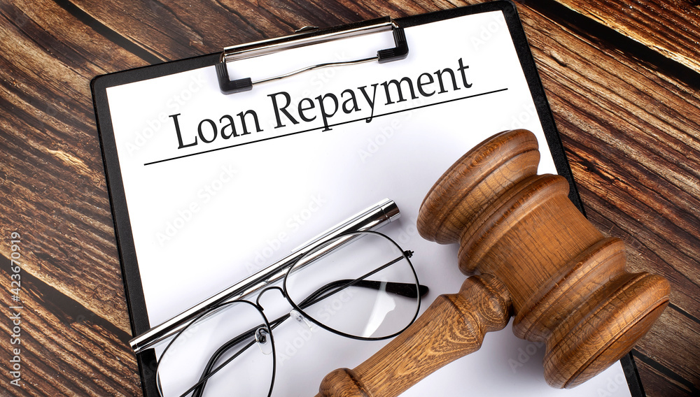 Paper with Loan Repayment with gavel, pen and glasses on wooden background Paper with Loan Repayment with gavel, pen and glasses on wooden background