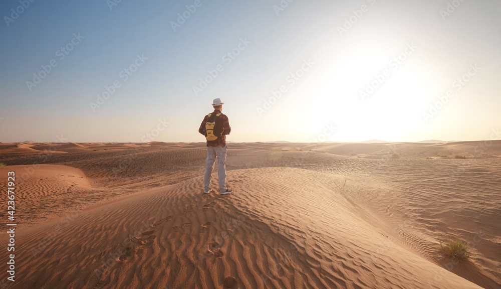 Desert adventure. Young man with backpack walking on sand dune. Dubai, United Arab Emirates