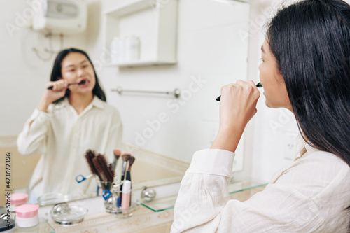 Young woman looking at bathroom window when brushing teeth in the morning