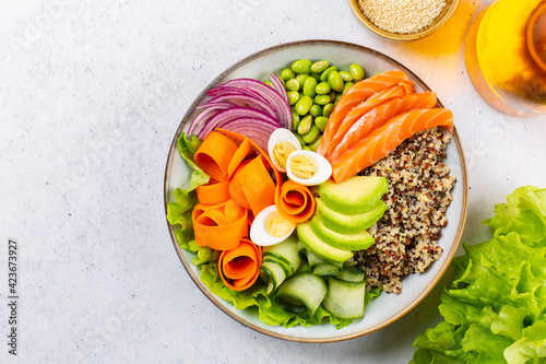 Buddha bowl with quail eggs and salmon, healthy food concept. Quinoa, edamame beans, avocado, ququmber, carrot, red onion and green salad. Light grey backgroud.