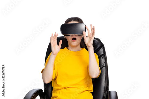 VR glasses. A young woman wearing virtual reality glasses, sitting in a chair and holding out her hands. White background. The concept of virtual reality © _KUBE_