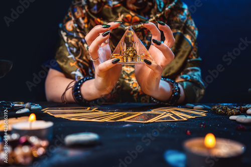 Witchcraft. The witch held a pyramid in her hands and worked magic on it. The tarot cards were on the table. Hands close-up. The concept of divination and astrology