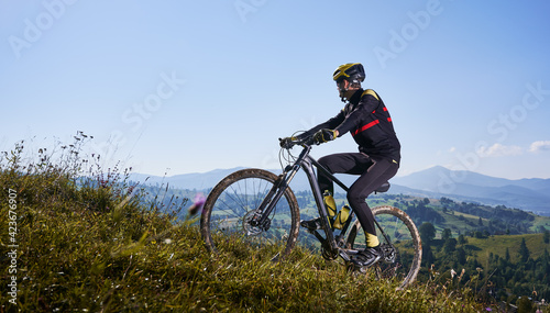 Joyful male cyclist riding bicycle uphill under blue sky.