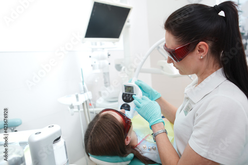 Profile shot of a female dentist wearing protective glasses, whitening teeth of patient with ultraviolet light