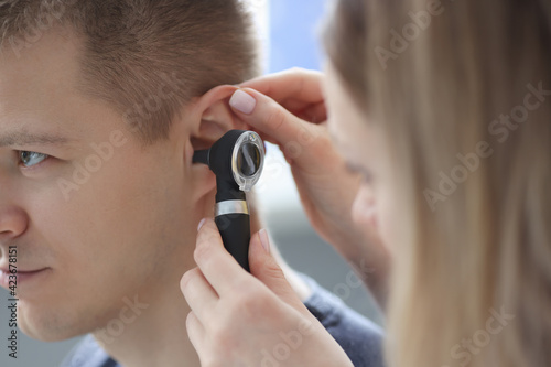 Doctor holding otoscope in his hand in front of patient ear closeup